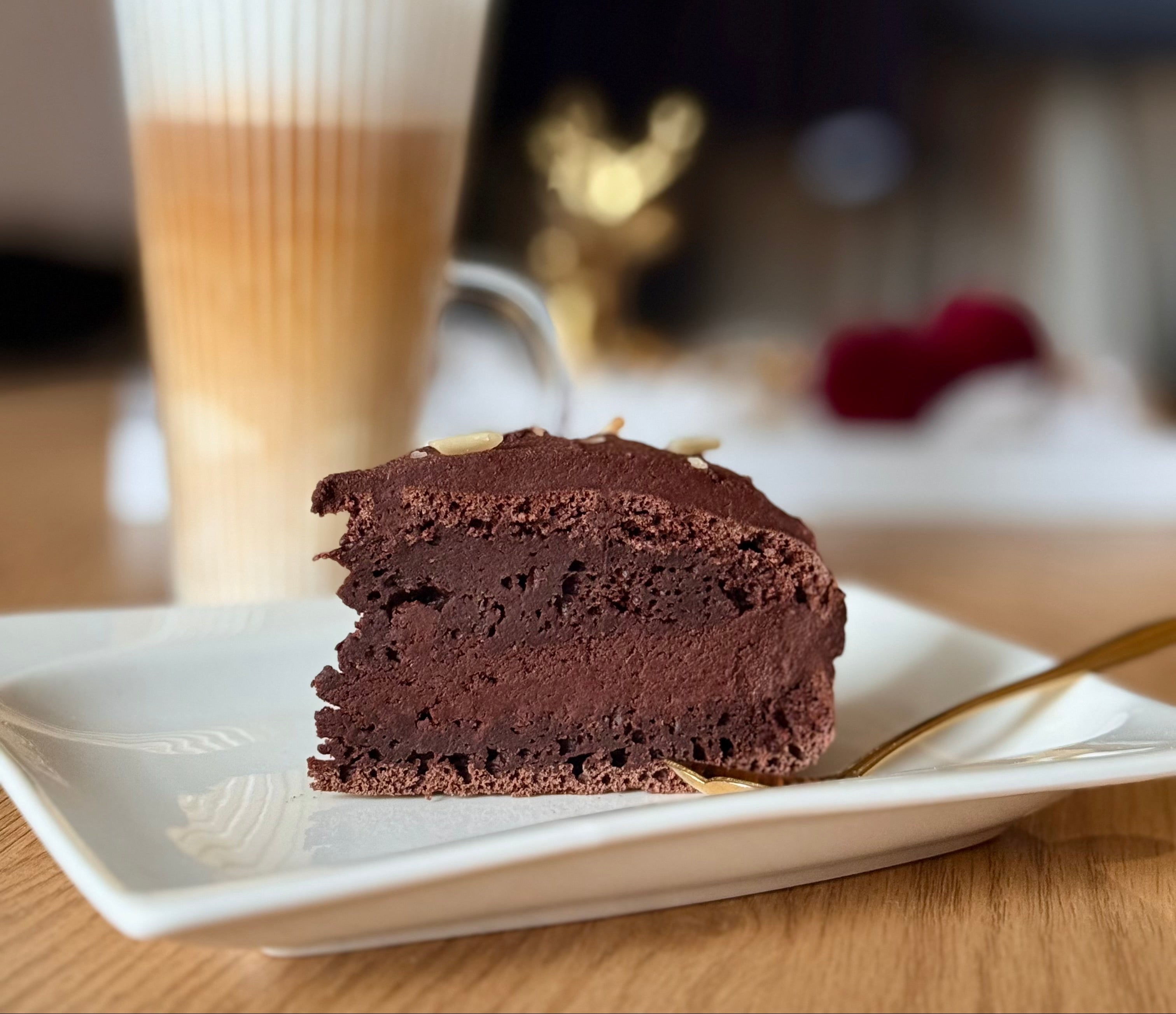 Slice of chocolate cake on a plate with a glass of iced coffee in the background
